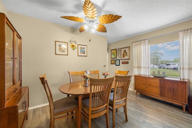 dining area with light wood-style floors, baseboards, a ceiling fan, and a textured ceiling