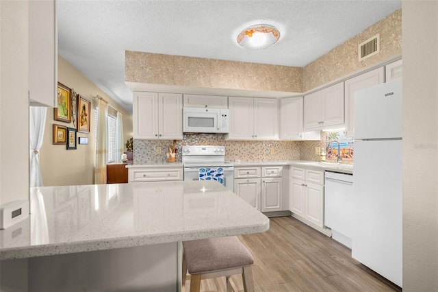 kitchen featuring light stone counters, white appliances, white cabinetry, light wood-style floors, and decorative backsplash