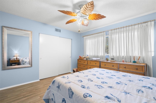 bedroom featuring a textured ceiling, wood finished floors, visible vents, baseboards, and a closet