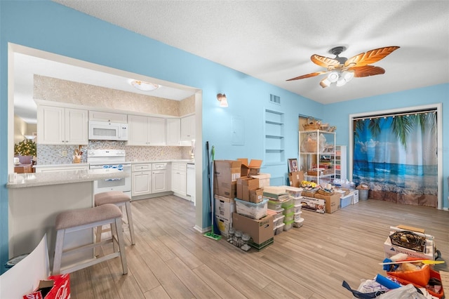 interior space featuring a textured ceiling, white appliances, visible vents, white cabinets, and light wood finished floors