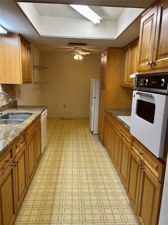 kitchen with white appliances, brown cabinetry, ceiling fan, light floors, and a sink