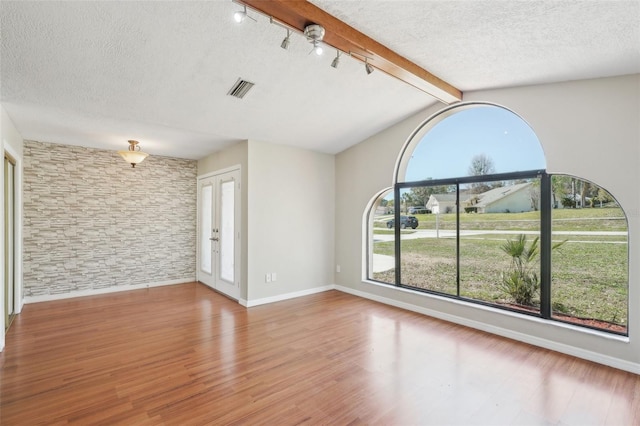 empty room with visible vents, a textured ceiling, wood finished floors, and vaulted ceiling with beams