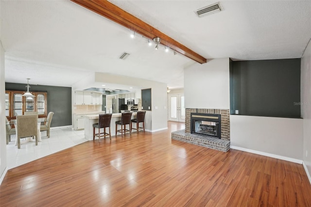 living area featuring lofted ceiling with beams, visible vents, and light wood-style flooring