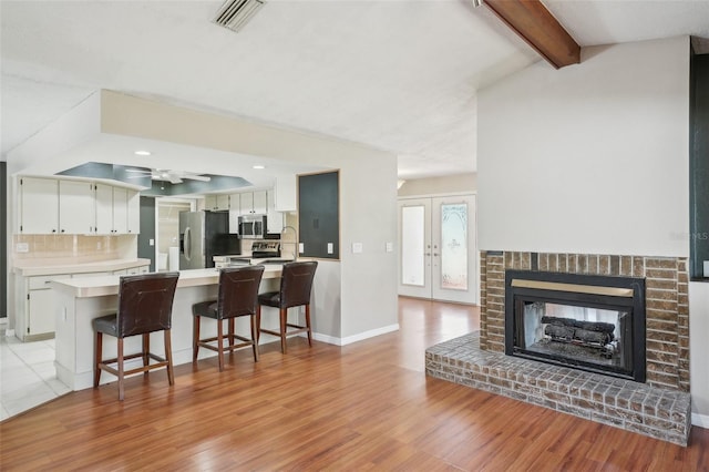 living room with a brick fireplace, vaulted ceiling with beams, visible vents, and light wood finished floors