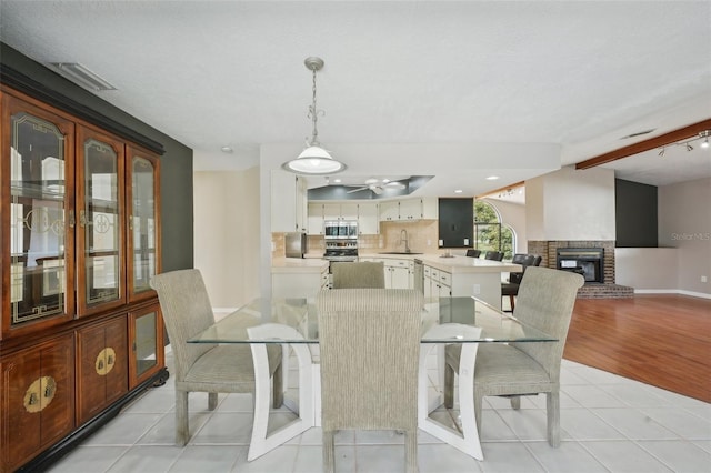 dining area with visible vents, vaulted ceiling with beams, a fireplace, light tile patterned flooring, and ceiling fan