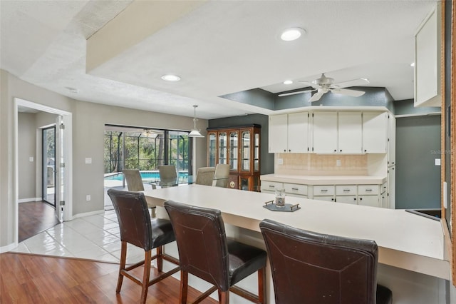 kitchen with a ceiling fan, a raised ceiling, light countertops, and tasteful backsplash