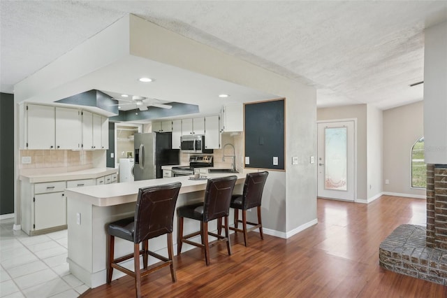 kitchen featuring a peninsula, decorative backsplash, light countertops, white cabinets, and appliances with stainless steel finishes