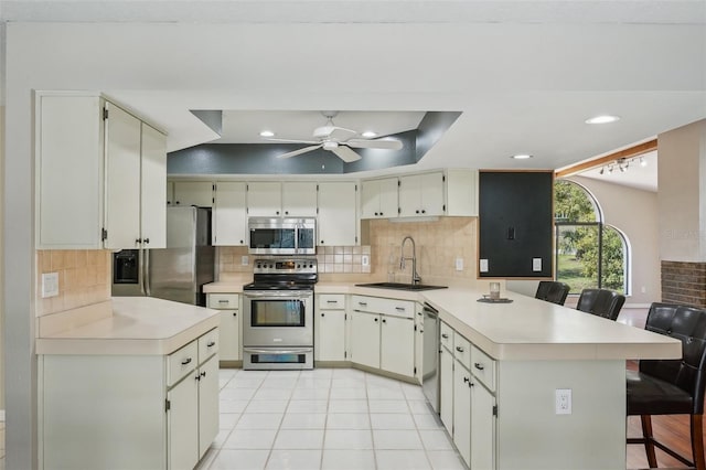 kitchen featuring a peninsula, a sink, decorative backsplash, light countertops, and appliances with stainless steel finishes