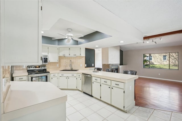 kitchen featuring appliances with stainless steel finishes, light countertops, a peninsula, and a sink