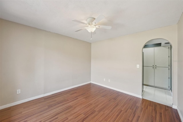 unfurnished room with a ceiling fan, a textured ceiling, wood finished floors, arched walkways, and baseboards