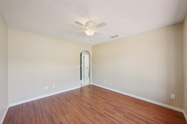 empty room with visible vents, baseboards, wood finished floors, arched walkways, and a ceiling fan