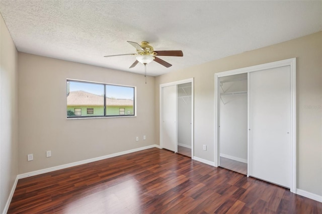 unfurnished bedroom featuring wood finished floors, baseboards, ceiling fan, a textured ceiling, and two closets