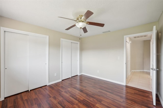 unfurnished bedroom featuring baseboards, wood finished floors, visible vents, and multiple closets