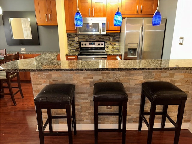 kitchen featuring dark wood-style floors, decorative backsplash, a breakfast bar area, and stainless steel appliances