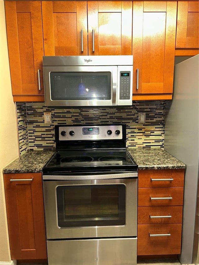 kitchen with brown cabinetry, backsplash, stainless steel appliances, and dark stone counters