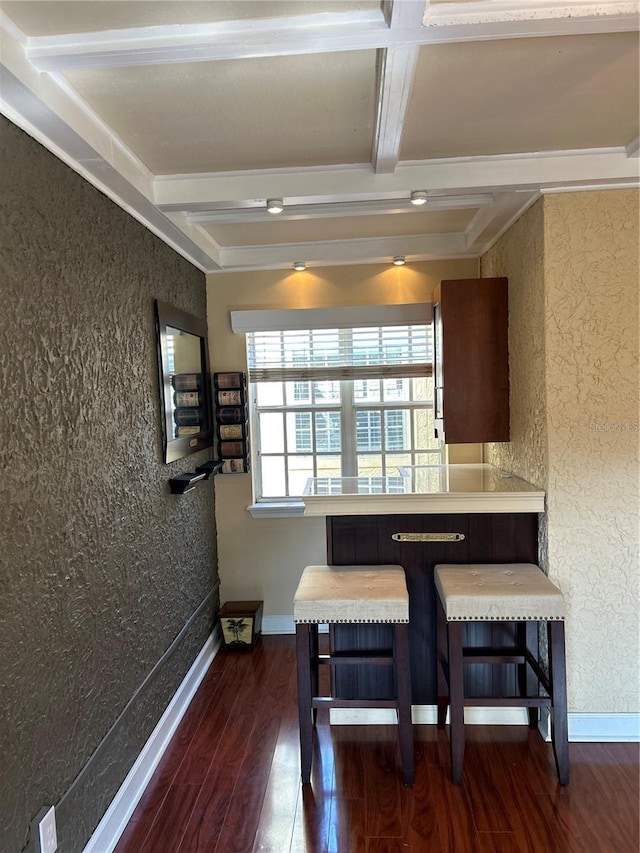 kitchen with dark wood-style floors, beamed ceiling, baseboards, a kitchen breakfast bar, and a textured wall