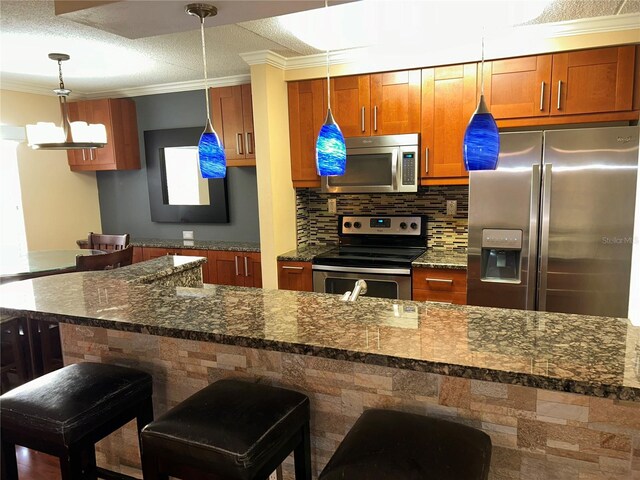 kitchen featuring ornamental molding, a kitchen breakfast bar, tasteful backsplash, stainless steel appliances, and hanging light fixtures