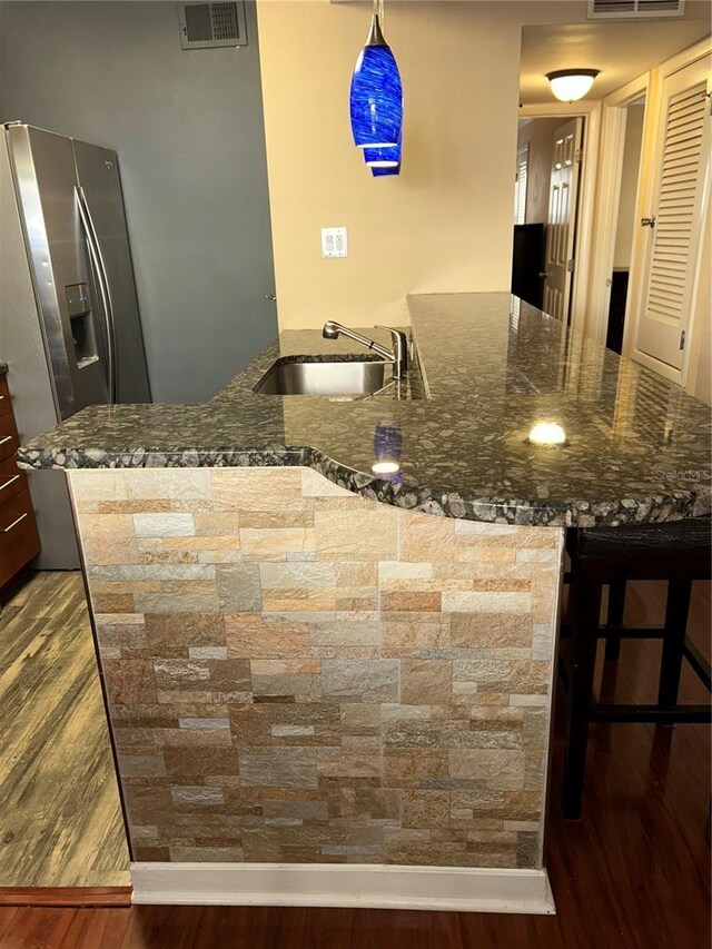 kitchen with visible vents, dark wood-type flooring, stainless steel fridge with ice dispenser, dark stone counters, and a sink