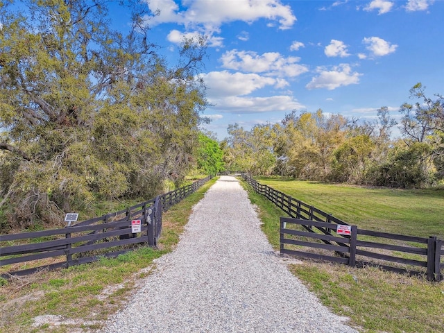 surrounding community featuring a rural view, a lawn, driveway, and fence