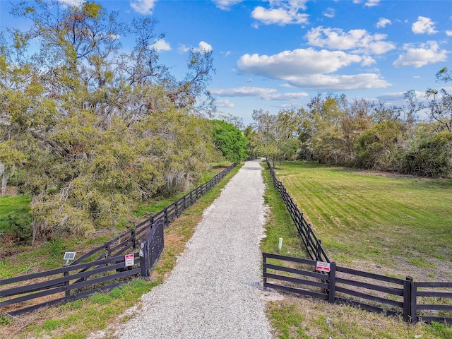 view of community featuring a rural view, fence, driveway, and a lawn