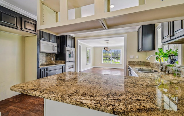 kitchen with multiple ovens, a sink, light stone counters, tasteful backsplash, and white microwave