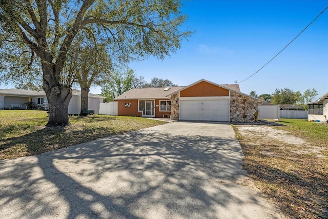 view of front of home with concrete driveway, a front yard, fence, a garage, and stone siding