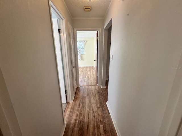 corridor with a textured ceiling, ornamental molding, dark wood finished floors, and baseboards