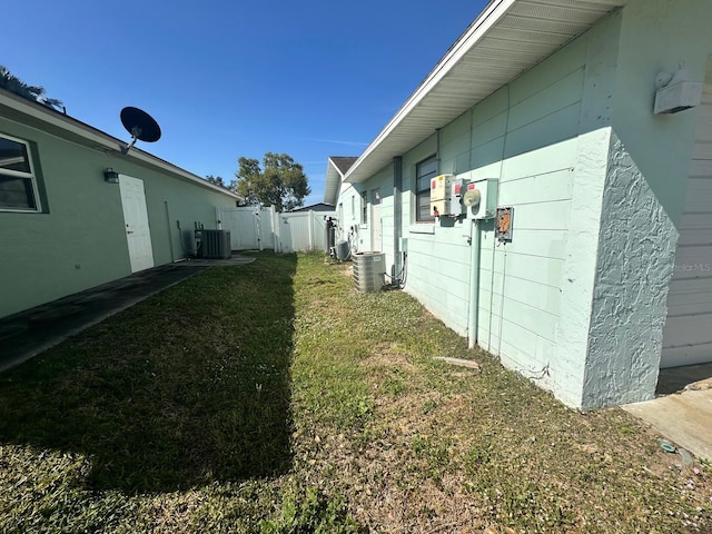 view of property exterior featuring stucco siding, fence, central AC, and a yard