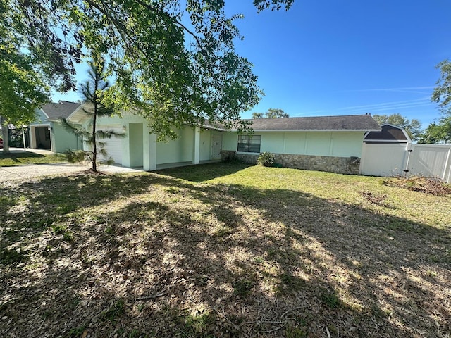 exterior space with a garage, fence, stone siding, a yard, and a gate