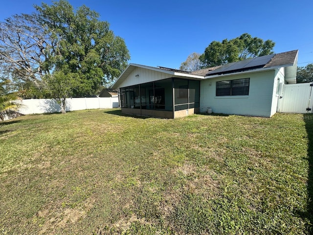 rear view of house featuring a sunroom, a fenced backyard, roof mounted solar panels, and a lawn