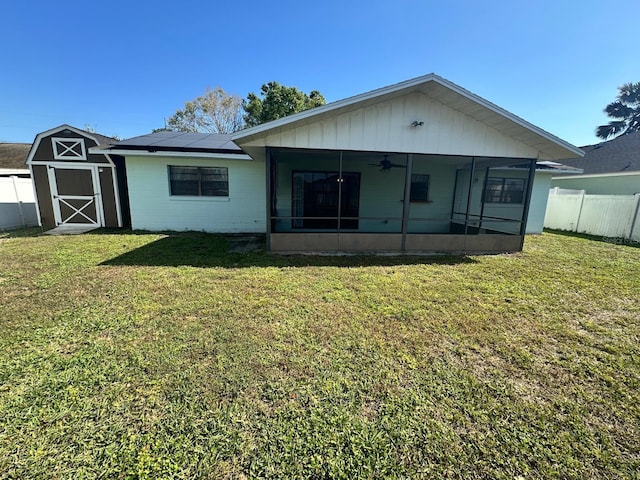 rear view of property featuring fence, a sunroom, a lawn, roof mounted solar panels, and a shed