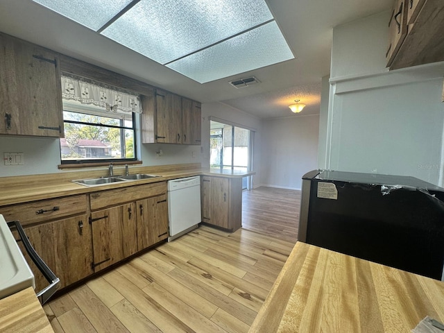 kitchen with visible vents, light wood finished floors, a peninsula, white dishwasher, and a sink