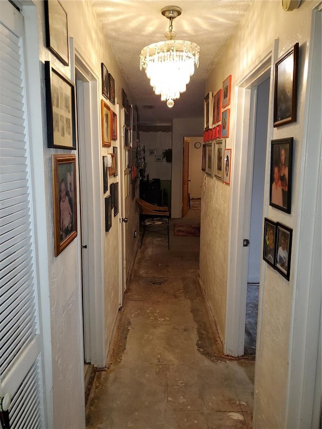 hallway with a chandelier, a textured wall, a textured ceiling, and concrete flooring