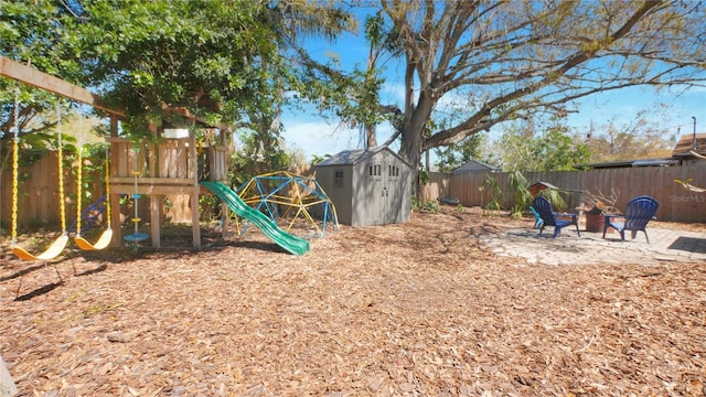 view of playground featuring an outbuilding, a shed, an outdoor fire pit, and a fenced backyard