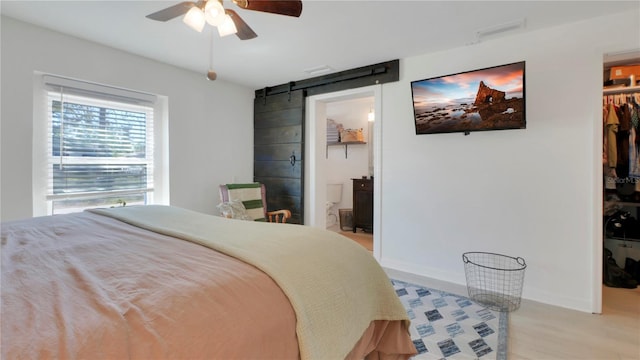 bedroom featuring a barn door, baseboards, a spacious closet, a closet, and light wood finished floors