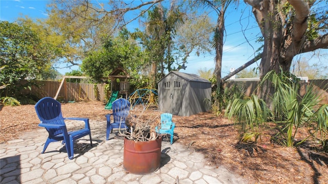 view of patio with a storage shed, a fenced backyard, a playground, and an outbuilding