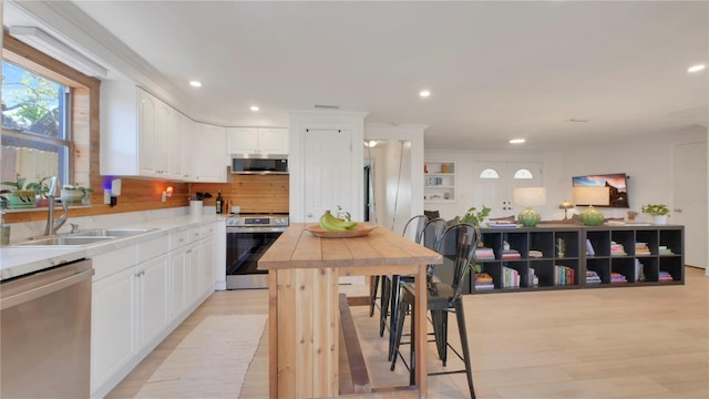 kitchen with recessed lighting, stainless steel appliances, a sink, white cabinets, and light wood finished floors