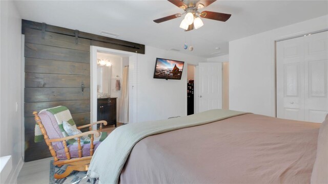 bedroom featuring a ceiling fan, ensuite bathroom, and a barn door