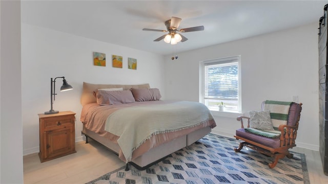 bedroom with ceiling fan, a barn door, light wood-type flooring, and baseboards