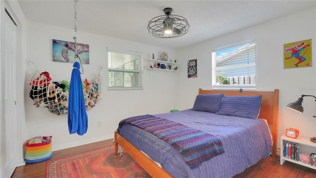 bedroom with multiple windows, a textured ceiling, baseboards, and wood finished floors