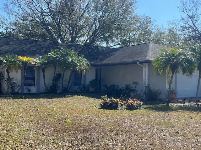 view of side of property featuring a yard, stucco siding, a garage, and roof with shingles