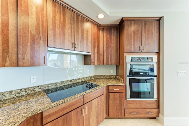 kitchen with light tile patterned floors, stone counters, black electric cooktop, under cabinet range hood, and double oven