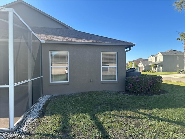 view of side of home featuring a lanai, roof with shingles, a lawn, and stucco siding