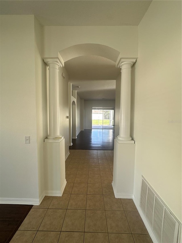 corridor with arched walkways, ornate columns, visible vents, baseboards, and tile patterned floors