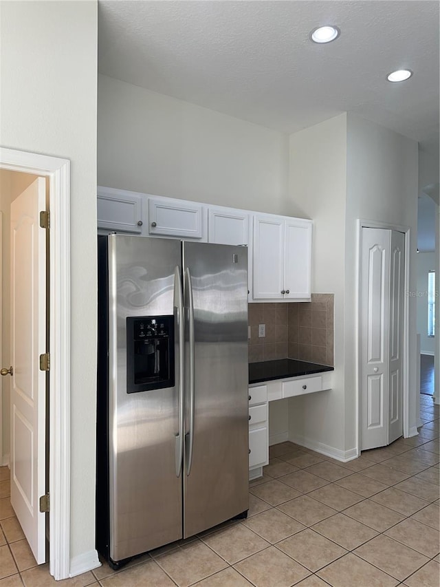 kitchen featuring light tile patterned floors, white cabinetry, built in study area, tasteful backsplash, and stainless steel fridge