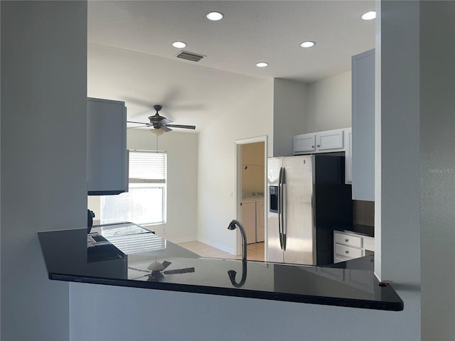 kitchen with stainless steel refrigerator with ice dispenser, washer and clothes dryer, dark countertops, visible vents, and a peninsula