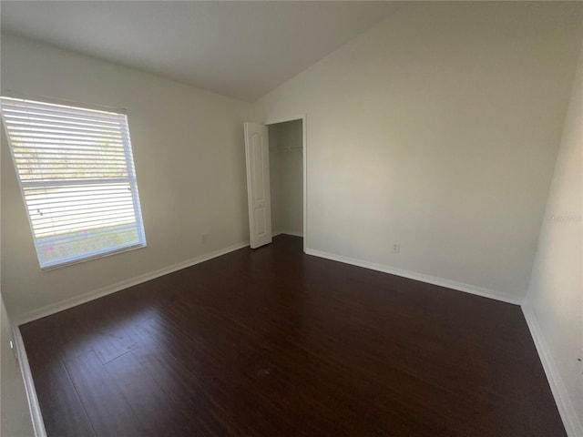 empty room featuring dark wood-style flooring, vaulted ceiling, and baseboards