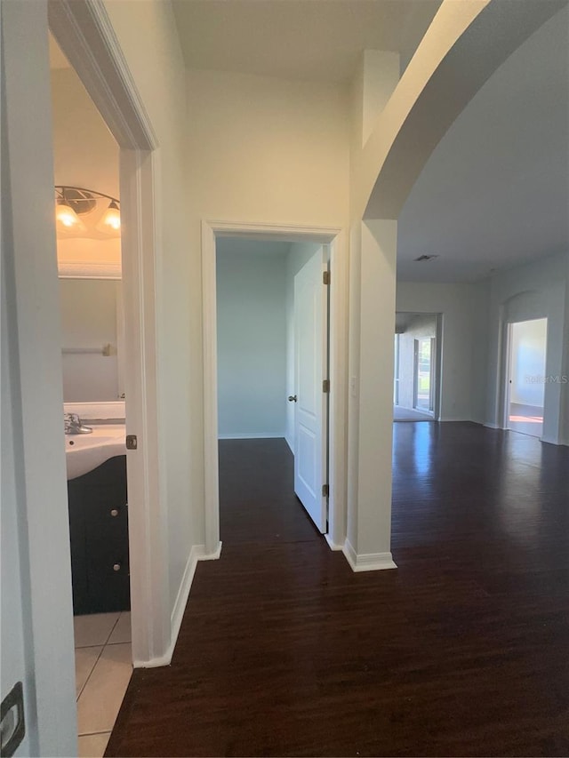 corridor featuring baseboards, arched walkways, and wood finished floors