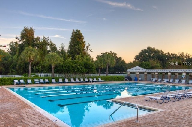 pool at dusk with a patio area, fence, and a community pool