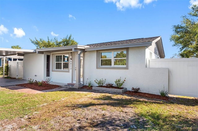 ranch-style home with a carport, a front yard, fence, and stucco siding